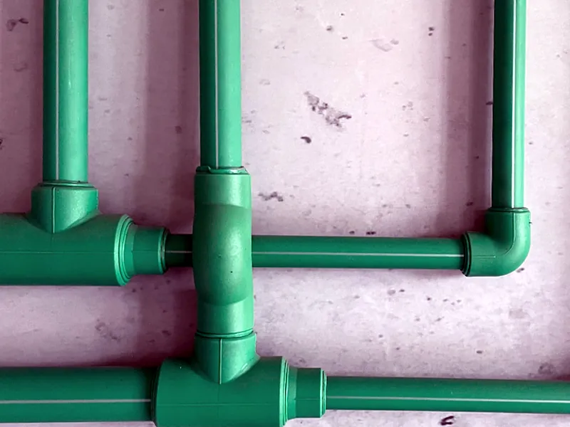 Cañerías de agua de termofusión verdes con uniones T y codos sobre una pared de obra